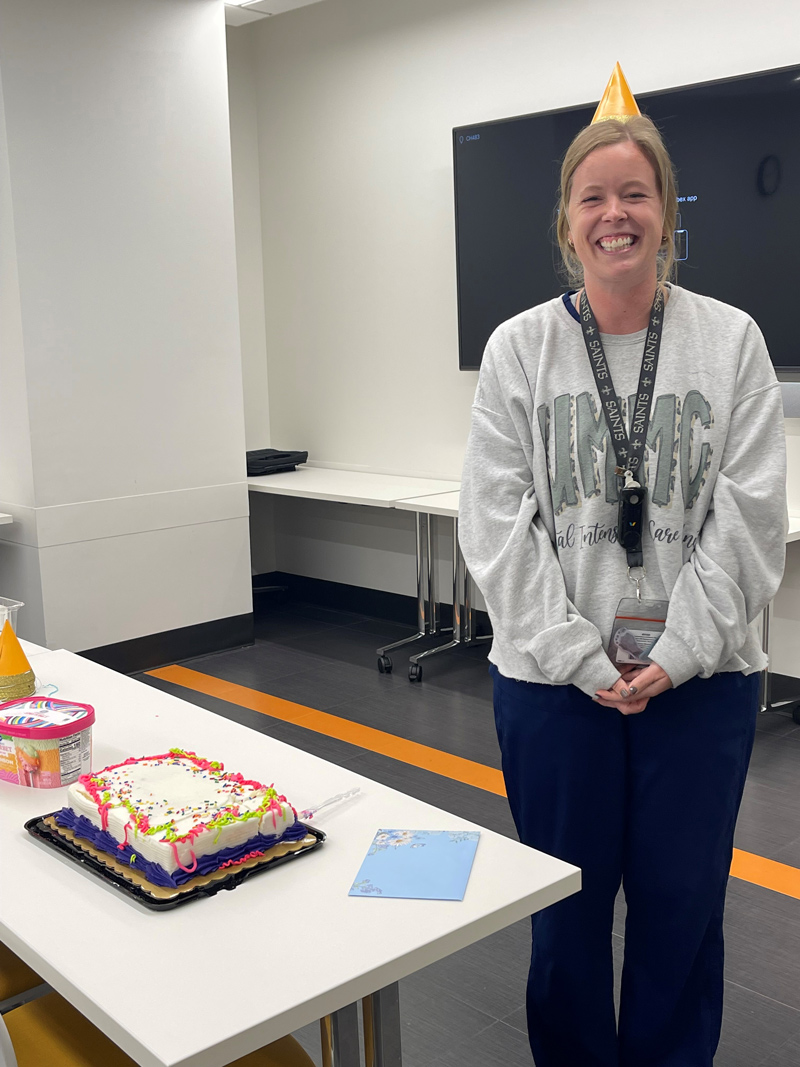 Smiling medical student wearing birthday hat and standing next to a table with a birthday, birthday card, and carton of ice cream.